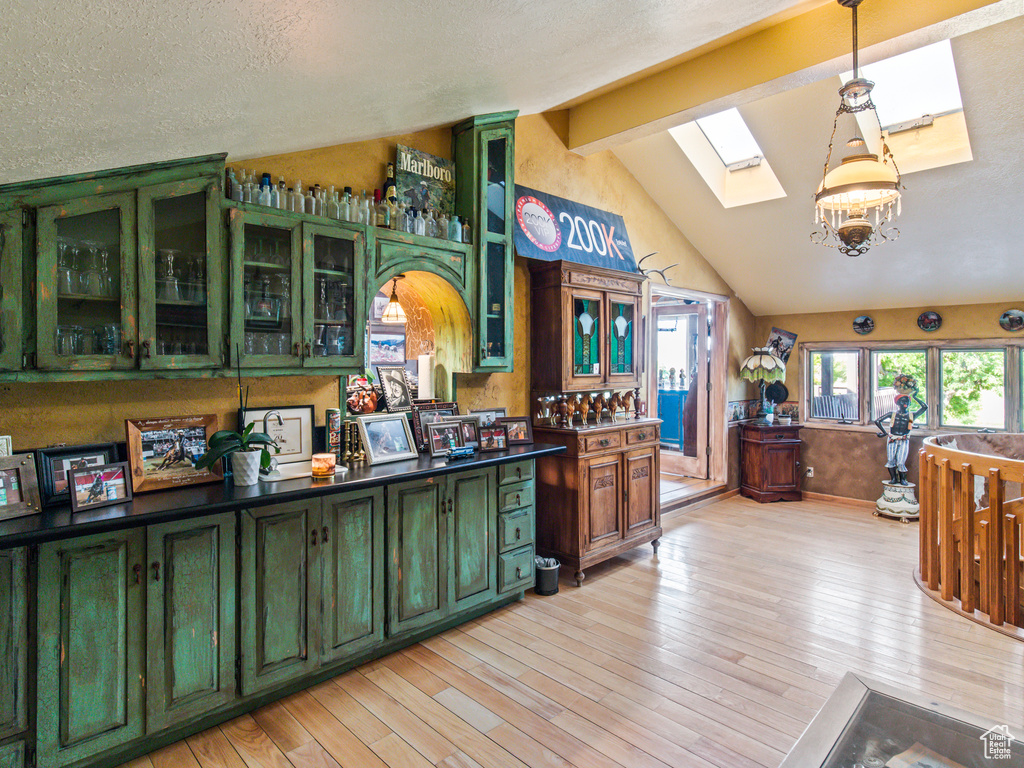 Kitchen featuring lofted ceiling with skylight, light hardwood / wood-style flooring, a textured ceiling, green cabinetry, and pendant lighting