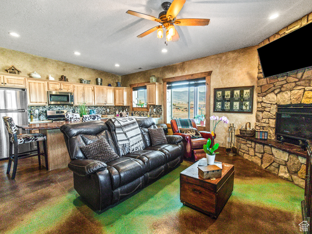 Living room featuring a fireplace, a textured ceiling, and ceiling fan