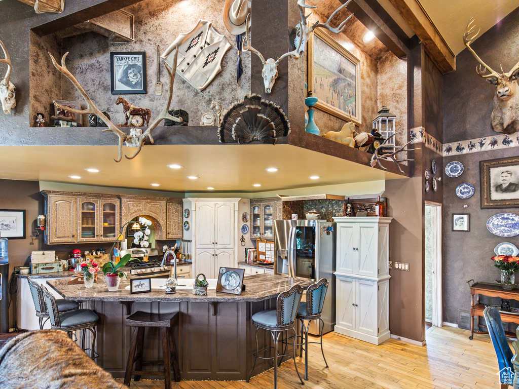 Kitchen with a kitchen bar, stone counters, light hardwood / wood-style flooring, stainless steel fridge with ice dispenser, and a center island