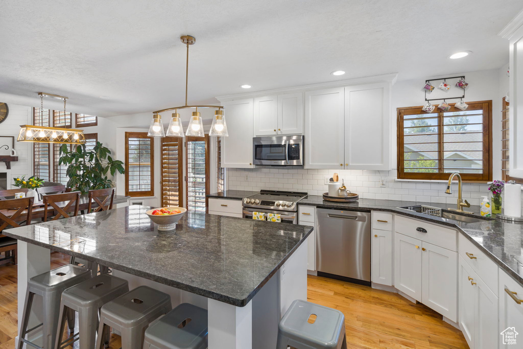 Kitchen featuring stainless steel appliances, sink, backsplash, light wood-type flooring, and a center island