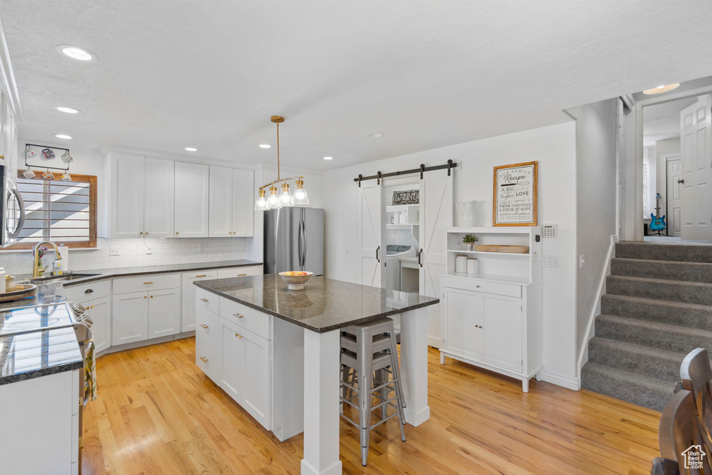 Kitchen with stainless steel appliances, a kitchen island, light hardwood / wood-style flooring, and a barn door