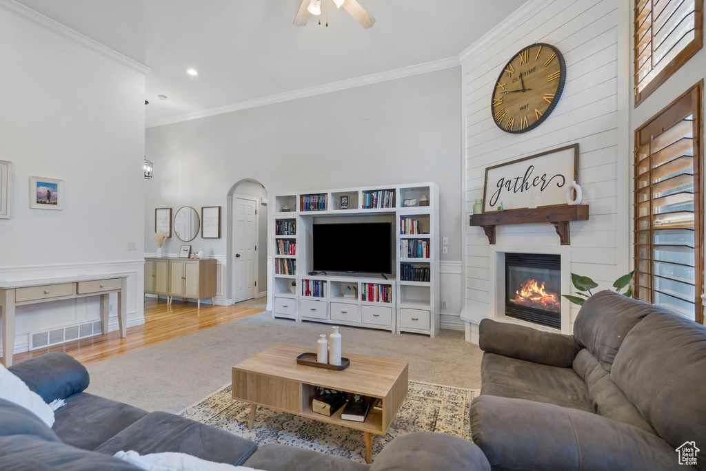 Living room with a fireplace, ceiling fan, light wood-type flooring, ornamental molding, and a towering ceiling