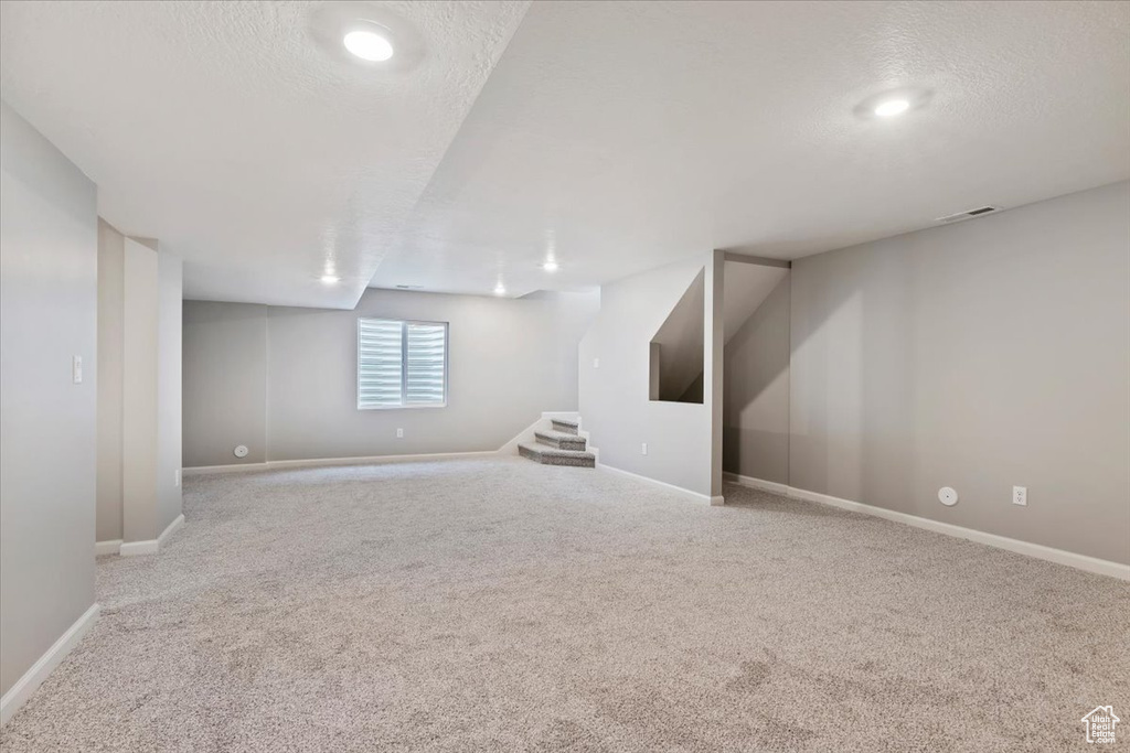 Basement with light colored carpet and a textured ceiling