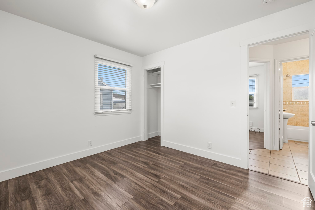 Unfurnished bedroom featuring ensuite bathroom, multiple windows, a closet, and hardwood / wood-style floors