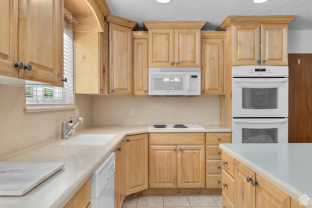 Kitchen featuring light tile patterned flooring, light brown cabinets, white appliances, and sink