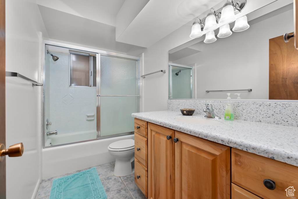 Full bathroom with vanity, tile patterned floors, toilet, and bath / shower combo with glass door
