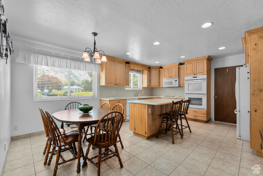 Kitchen featuring light tile patterned flooring, white appliances, an inviting chandelier, a center island, and decorative light fixtures