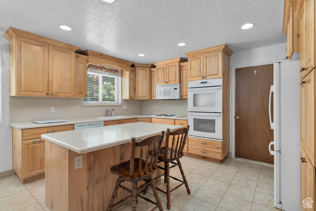 Kitchen featuring white appliances, light tile patterned floors, a kitchen island, a kitchen bar, and sink
