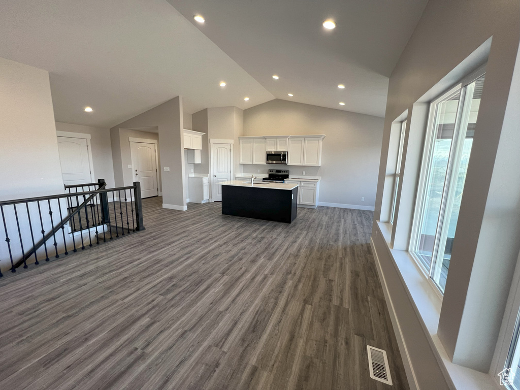 Kitchen featuring appliances with stainless steel finishes, white cabinets, a kitchen island with sink, lofted ceiling, and hardwood / wood-style flooring