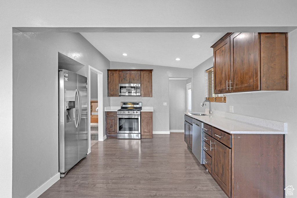 Kitchen featuring wood-type flooring, stainless steel appliances, sink, light stone counters, and lofted ceiling