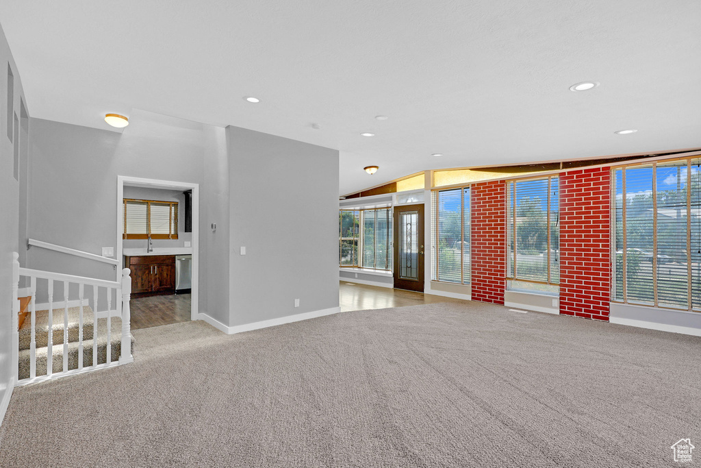 Unfurnished living room featuring sink, lofted ceiling, and light colored carpet