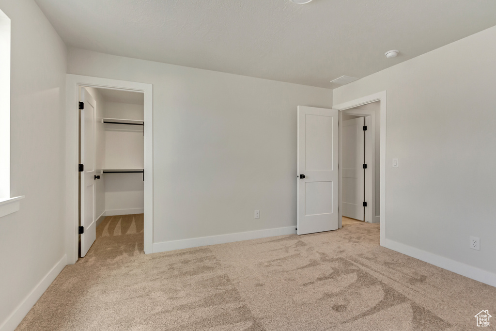 Unfurnished bedroom featuring a walk in closet, light carpet, and a closet