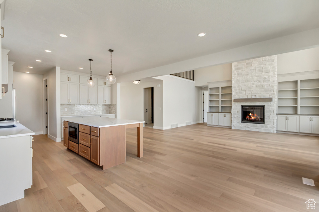 Kitchen with tasteful backsplash, decorative light fixtures, white cabinets, a kitchen island, and stainless steel microwave