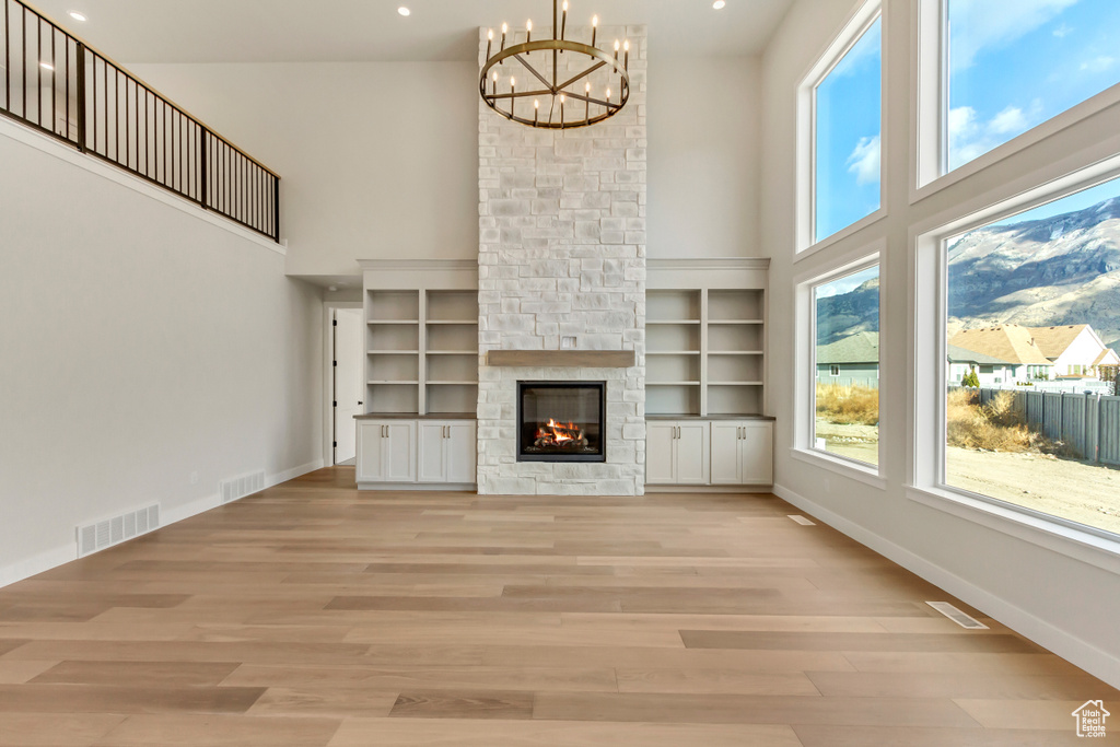 Unfurnished living room with light wood-type flooring, a fireplace, a high ceiling, and a chandelier