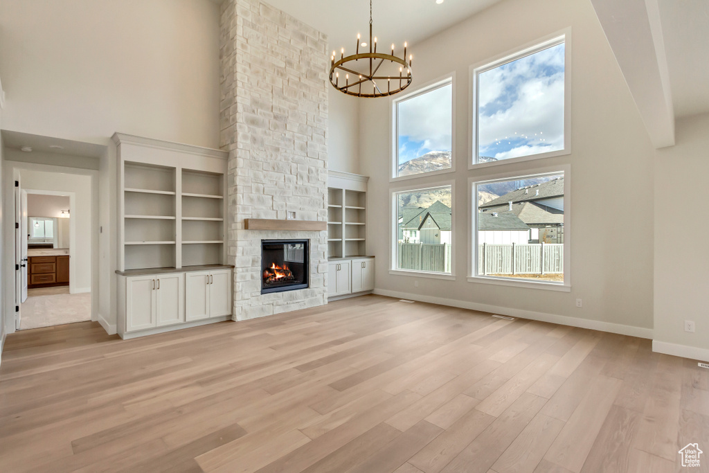 Unfurnished living room with a wealth of natural light, a fireplace, a towering ceiling, and light hardwood / wood-style floors