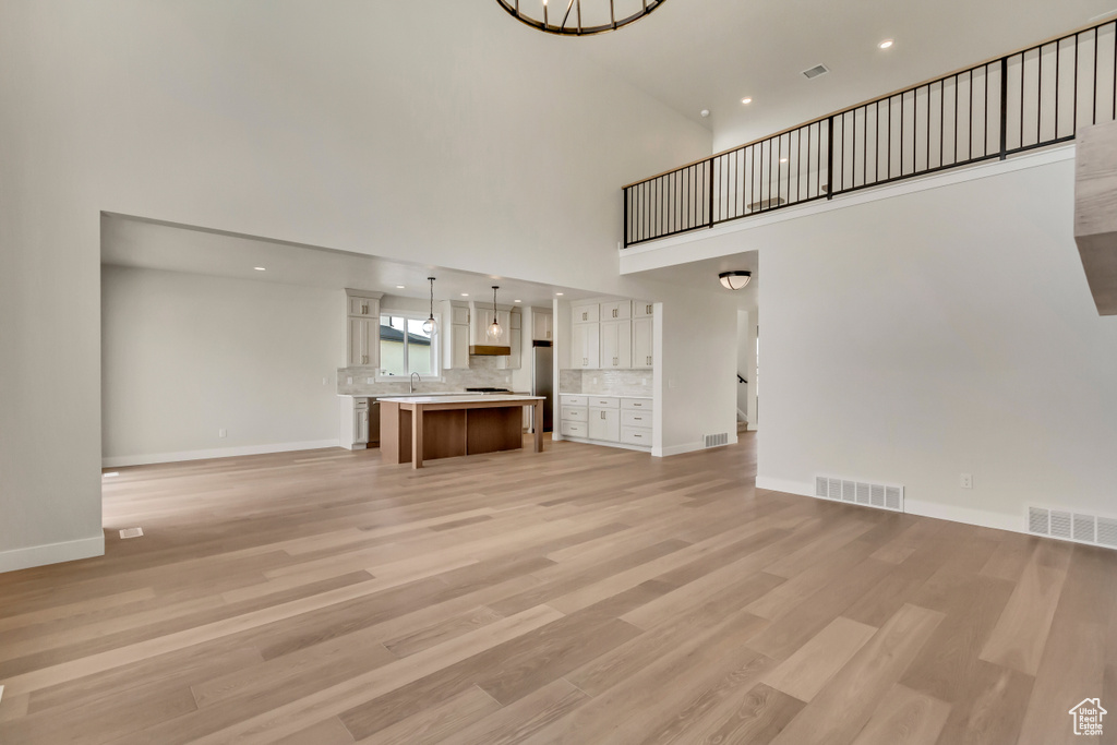 Unfurnished living room with a high ceiling, light wood-type flooring, and sink