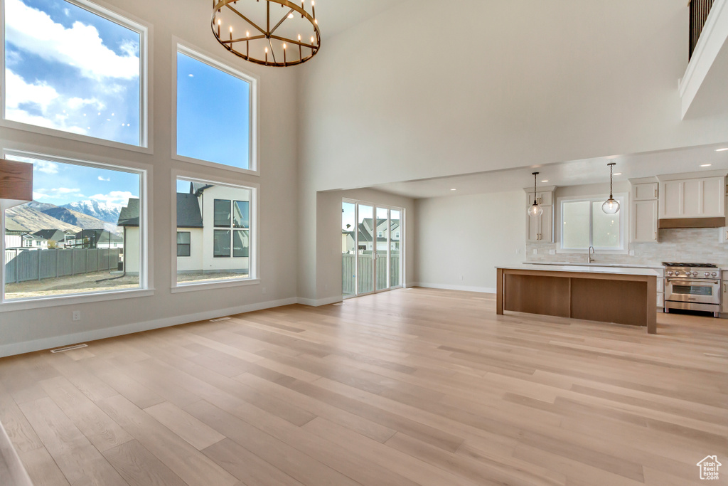 Unfurnished living room featuring plenty of natural light, a towering ceiling, and a notable chandelier