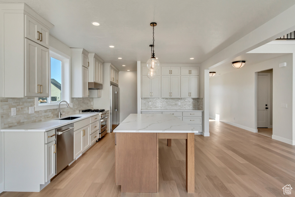 Kitchen with pendant lighting, a center island, high quality appliances, sink, and white cabinetry