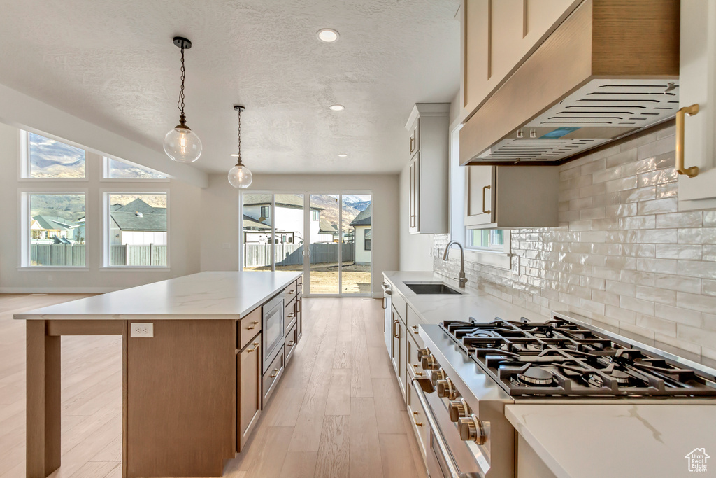 Kitchen with custom exhaust hood, high end stove, sink, decorative light fixtures, and a kitchen island