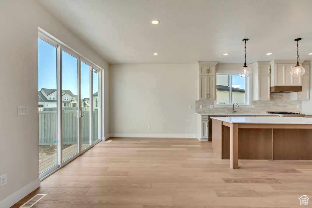 Kitchen featuring stainless steel range, sink, hanging light fixtures, tasteful backsplash, and light hardwood / wood-style floors