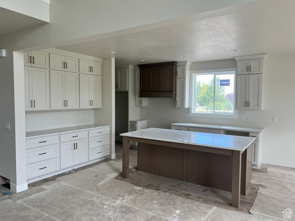 Kitchen with a textured ceiling, a center island, and light stone countertops