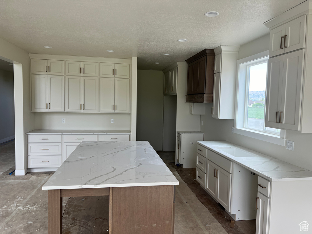 Kitchen featuring white cabinets, a center island, hardwood / wood-style floors, light stone countertops, and a textured ceiling