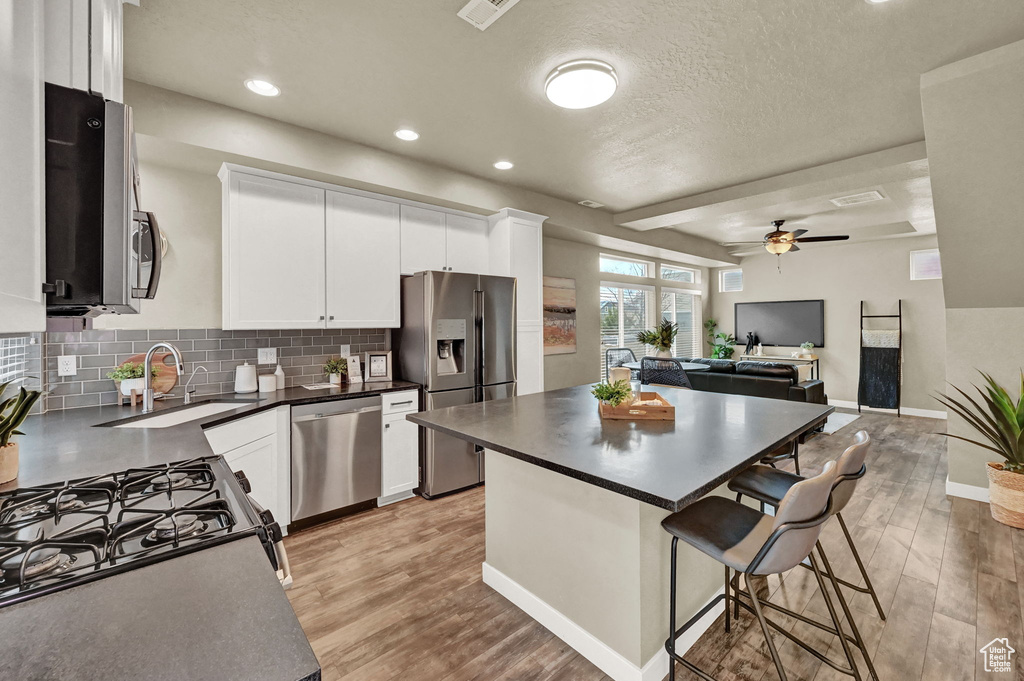 Kitchen featuring appliances with stainless steel finishes, light hardwood / wood-style flooring, backsplash, white cabinetry, and ceiling fan