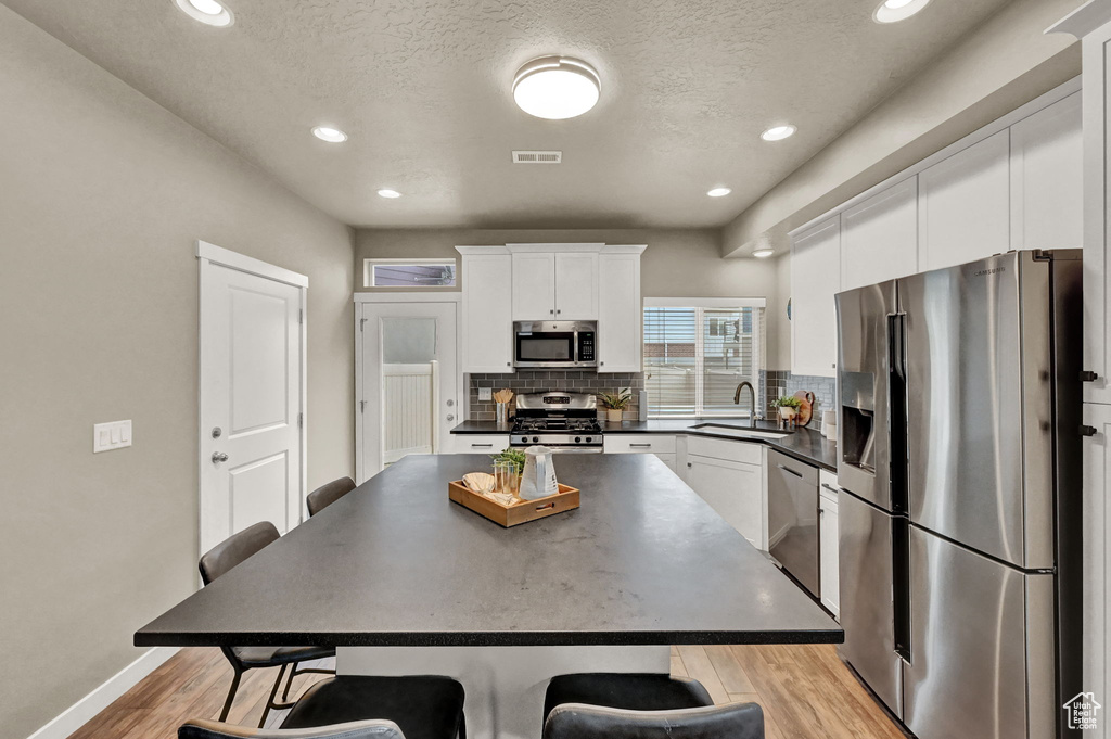 Kitchen featuring white cabinetry, backsplash, a kitchen island, light hardwood / wood-style floors, and appliances with stainless steel finishes