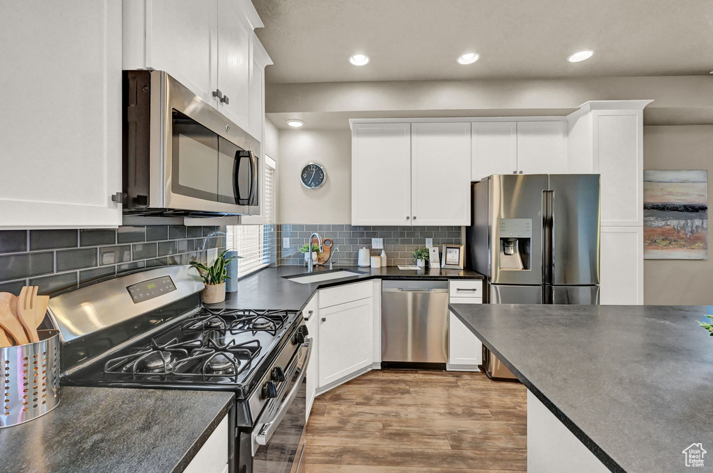 Kitchen with light hardwood / wood-style flooring, white cabinets, stainless steel appliances, decorative backsplash, and sink