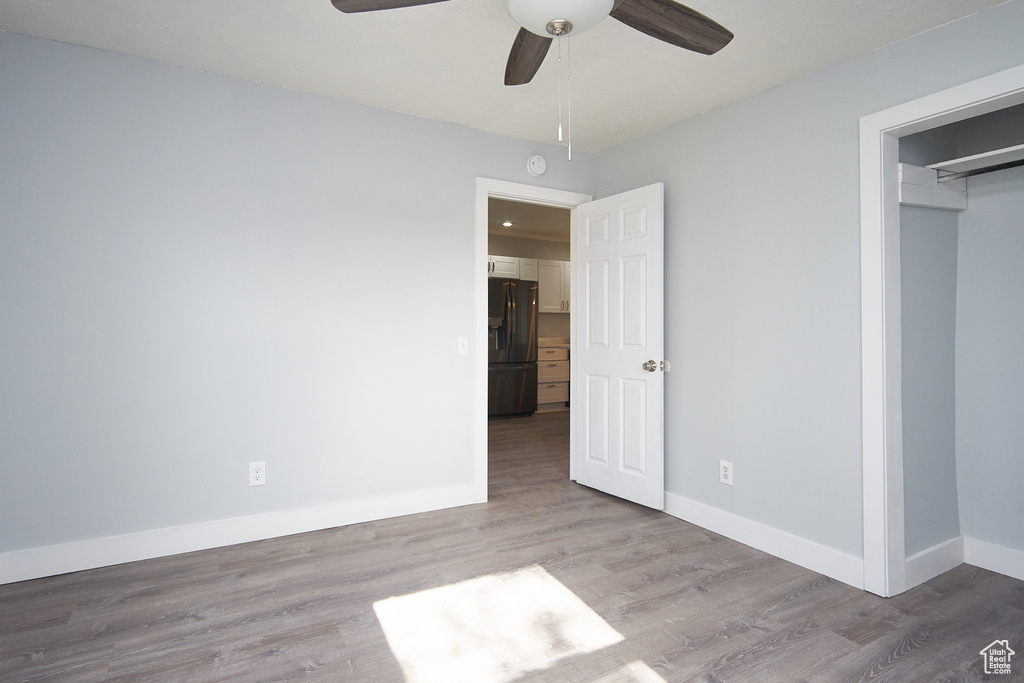 Unfurnished bedroom with ceiling fan, wood-type flooring, black refrigerator with ice dispenser, and a closet