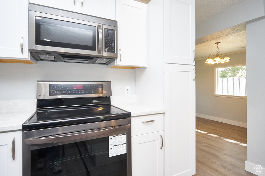 Kitchen featuring white cabinetry, a notable chandelier, light wood-type flooring, appliances with stainless steel finishes, and decorative light fixtures