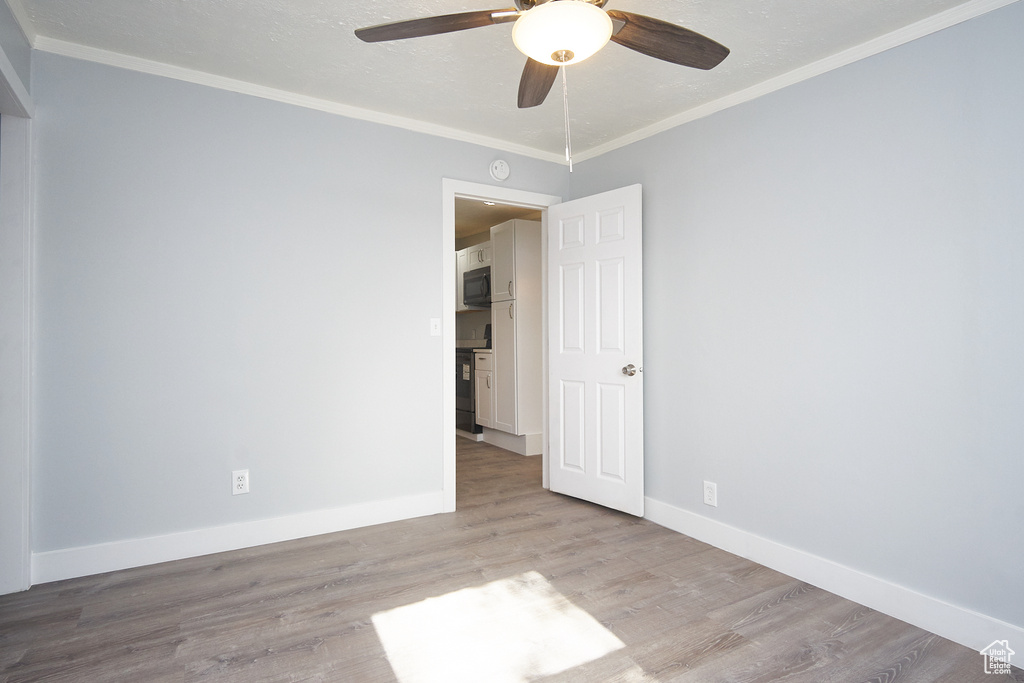 Spare room with crown molding, light wood-type flooring, and ceiling fan