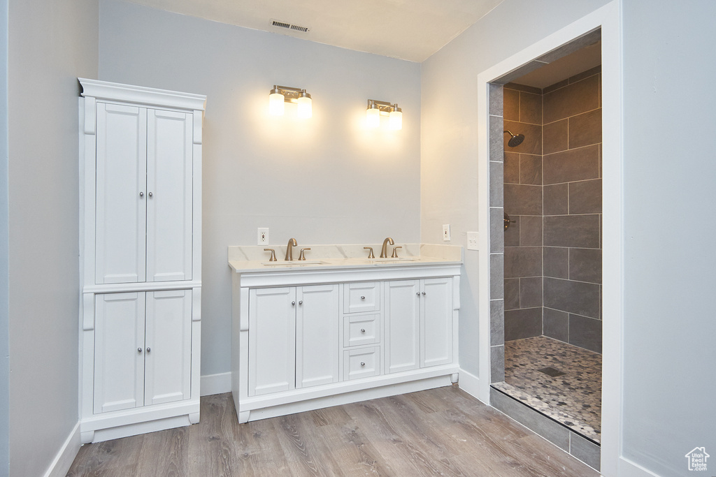 Bathroom with dual vanity, wood-type flooring, and a tile shower