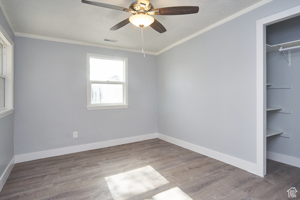 Unfurnished bedroom with a spacious closet, a closet, hardwood / wood-style floors, ceiling fan, and ornamental molding