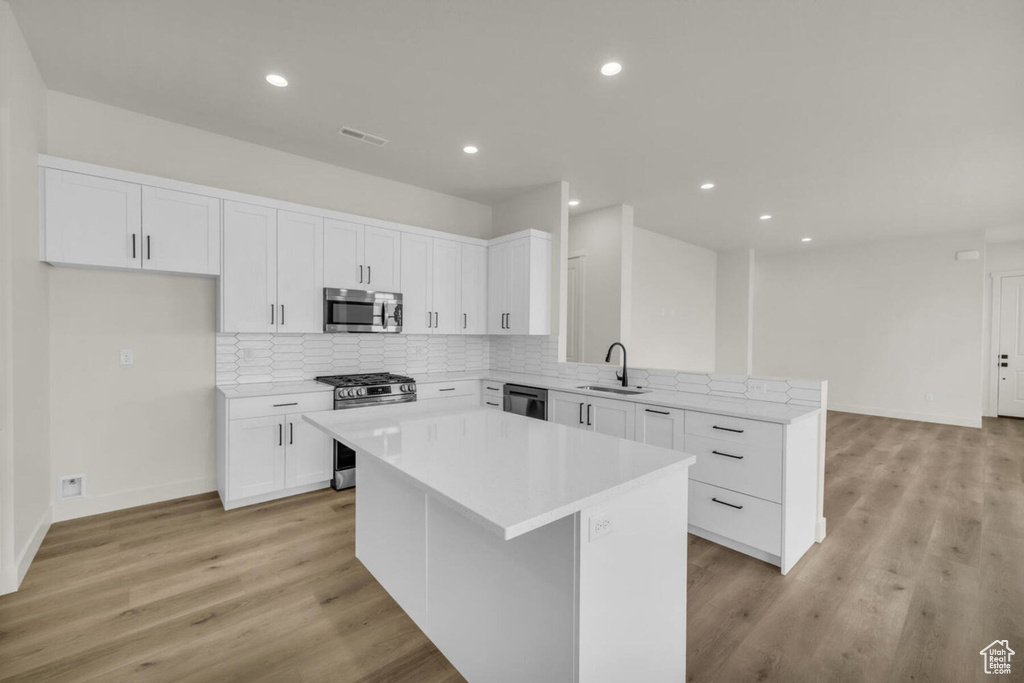 Kitchen featuring stainless steel appliances, white cabinets, sink, a kitchen island, and light wood-type flooring