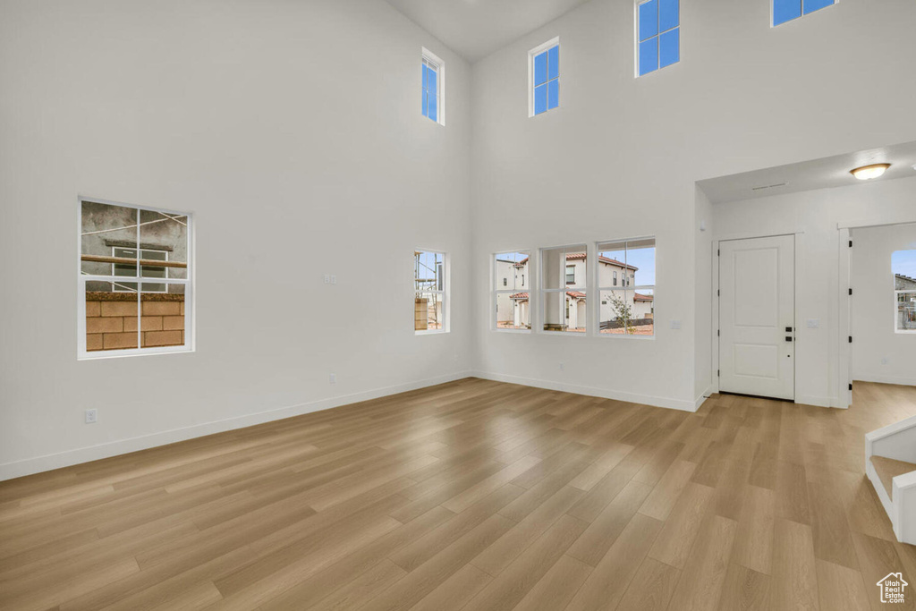 Unfurnished living room featuring light wood-type flooring and a towering ceiling