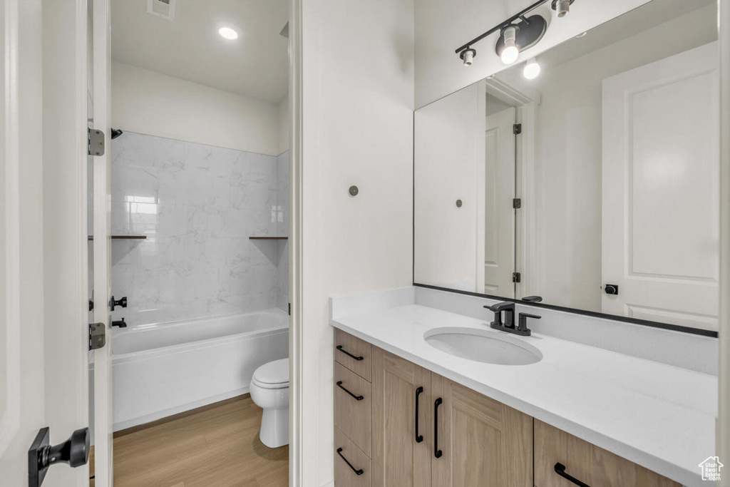 Full bathroom with wood-type flooring, toilet, vanity, and tiled shower / bath combo