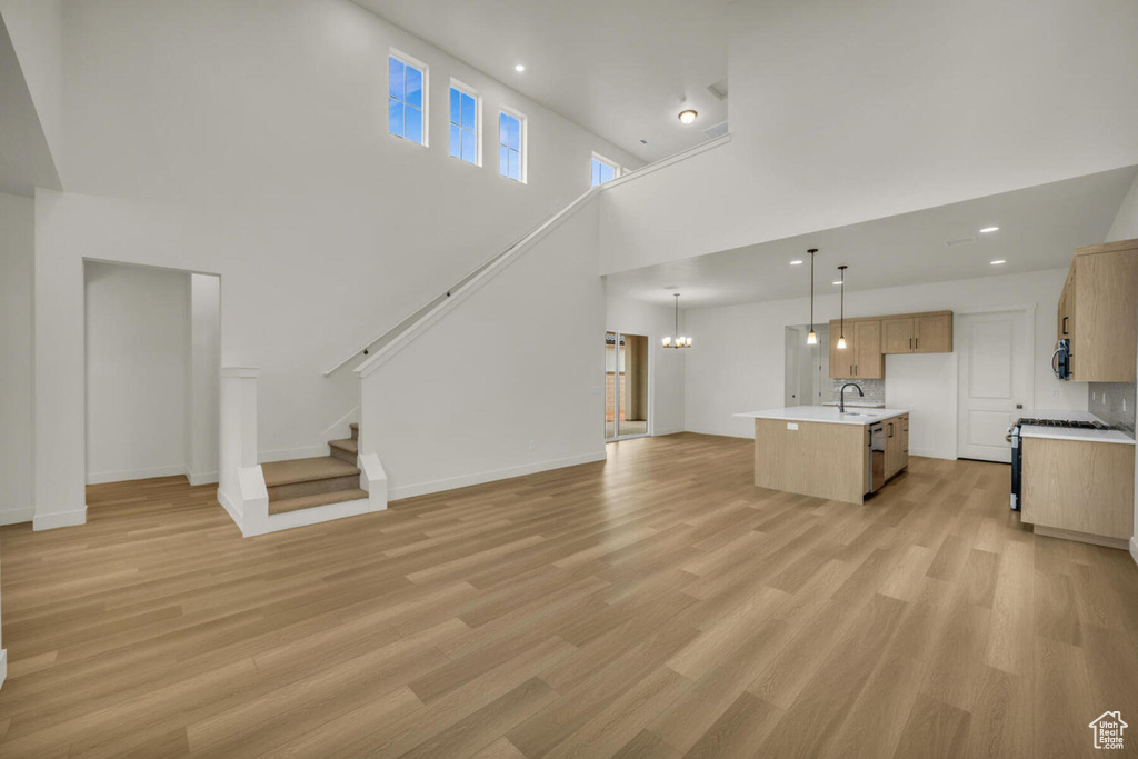 Unfurnished living room with light hardwood / wood-style floors, sink, a notable chandelier, and a high ceiling