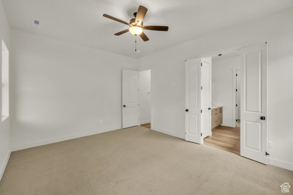 Unfurnished bedroom featuring ensuite bath, light colored carpet, and ceiling fan