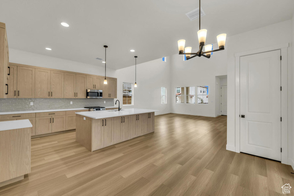 Kitchen with tasteful backsplash, light brown cabinets, light hardwood / wood-style floors, decorative light fixtures, and a center island with sink