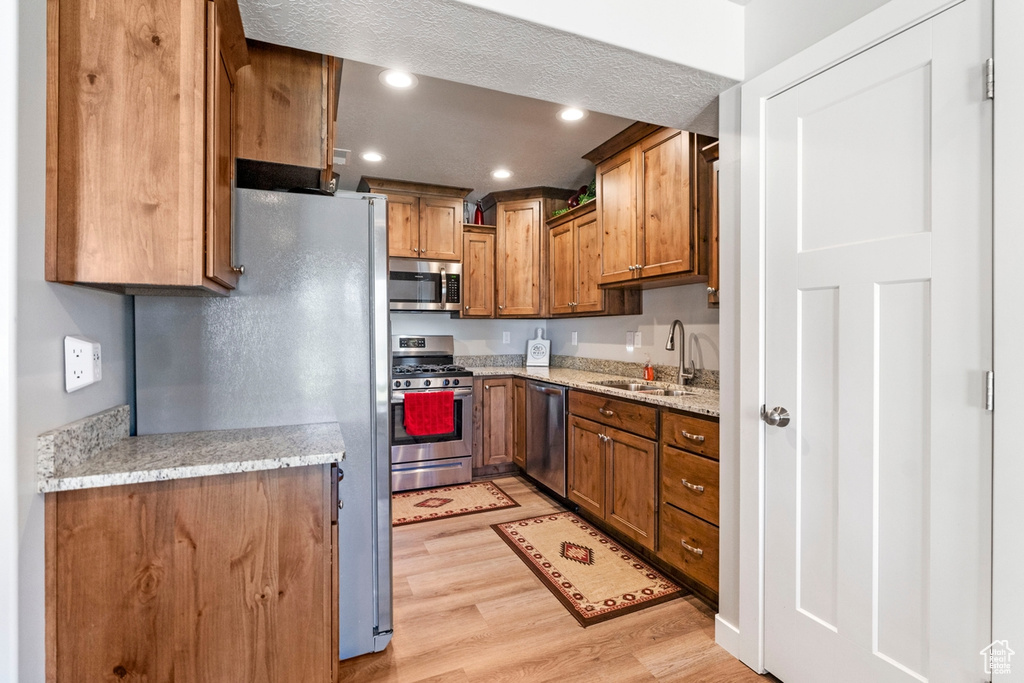 Kitchen featuring light hardwood / wood-style flooring, a textured ceiling, light stone counters, sink, and appliances with stainless steel finishes