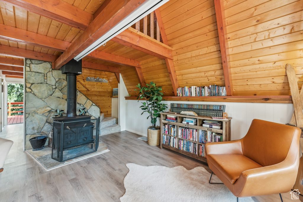 Living area featuring a wood stove, light wood-type flooring, beam ceiling, wood walls, and wooden ceiling