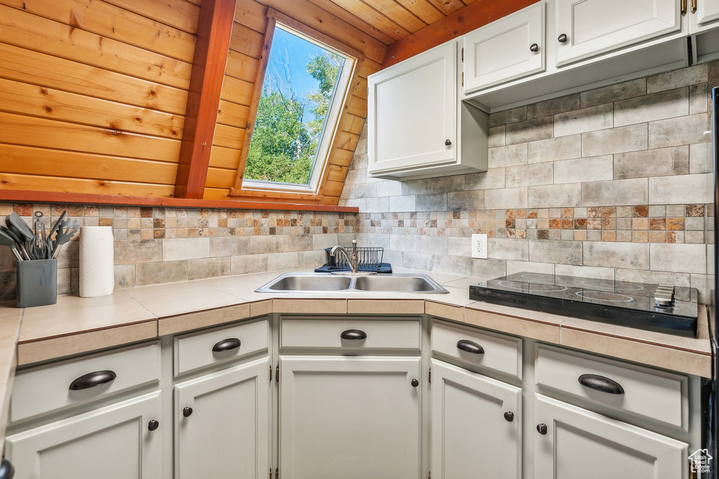 Kitchen featuring white cabinetry, lofted ceiling with skylight, tasteful backsplash, wooden ceiling, and sink