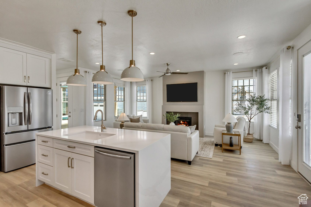 Kitchen with light hardwood / wood-style flooring, a kitchen island with sink, appliances with stainless steel finishes, pendant lighting, and sink