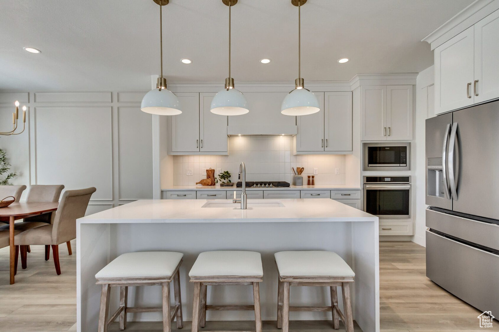 Kitchen featuring backsplash, decorative light fixtures, light hardwood / wood-style flooring, and appliances with stainless steel finishes