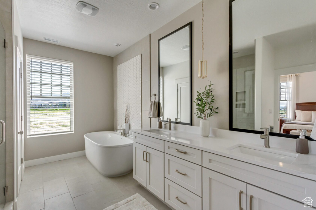 Bathroom featuring a washtub, a healthy amount of sunlight, tile patterned floors, and dual vanity