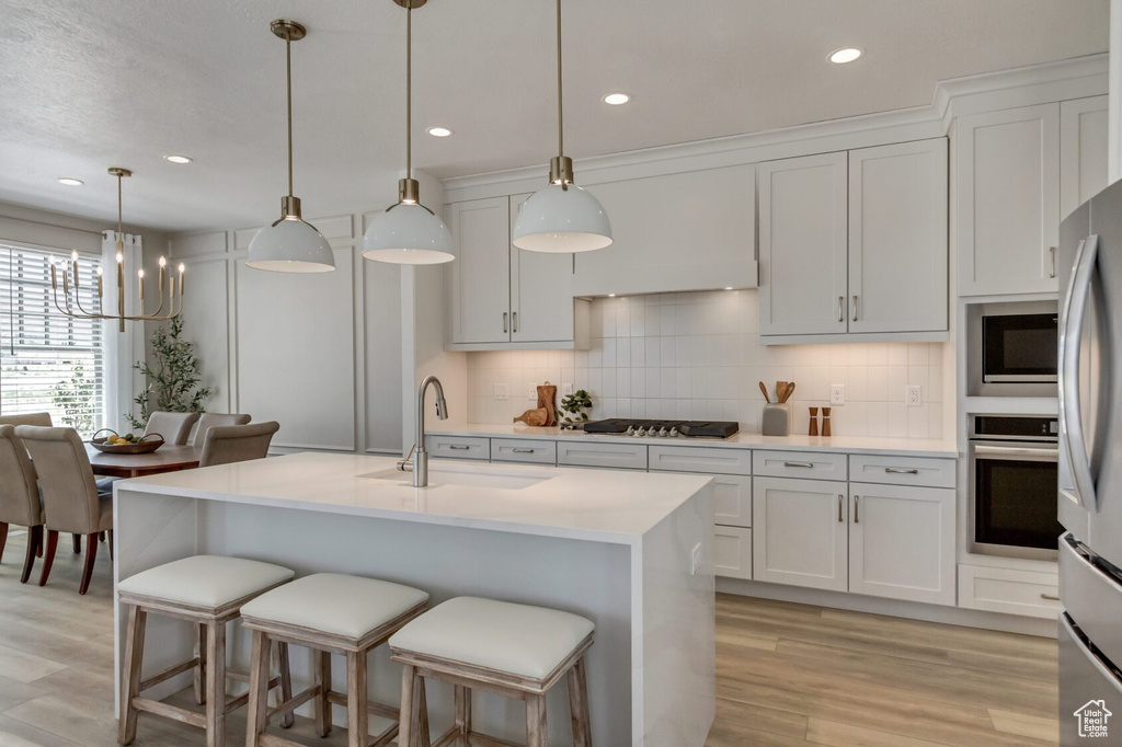 Kitchen featuring light hardwood / wood-style flooring, tasteful backsplash, stainless steel appliances, pendant lighting, and sink