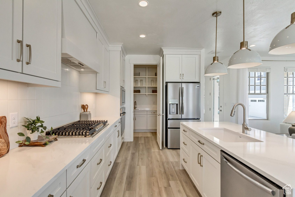 Kitchen featuring white cabinetry, light hardwood / wood-style flooring, tasteful backsplash, appliances with stainless steel finishes, and sink