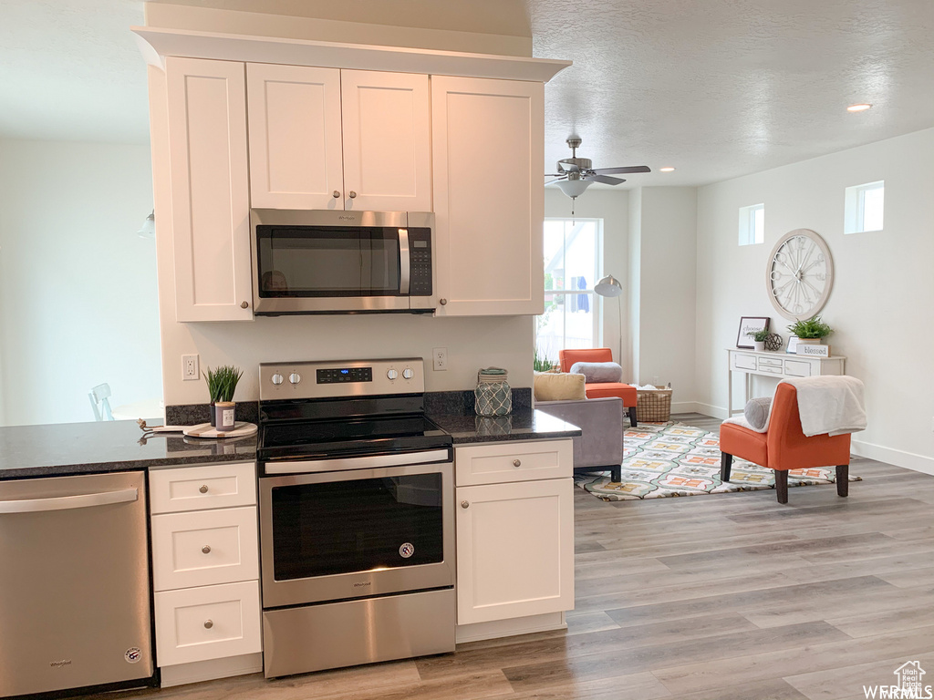 Kitchen with dark stone countertops, white cabinets, ceiling fan, light hardwood / wood-style floors, and appliances with stainless steel finishes