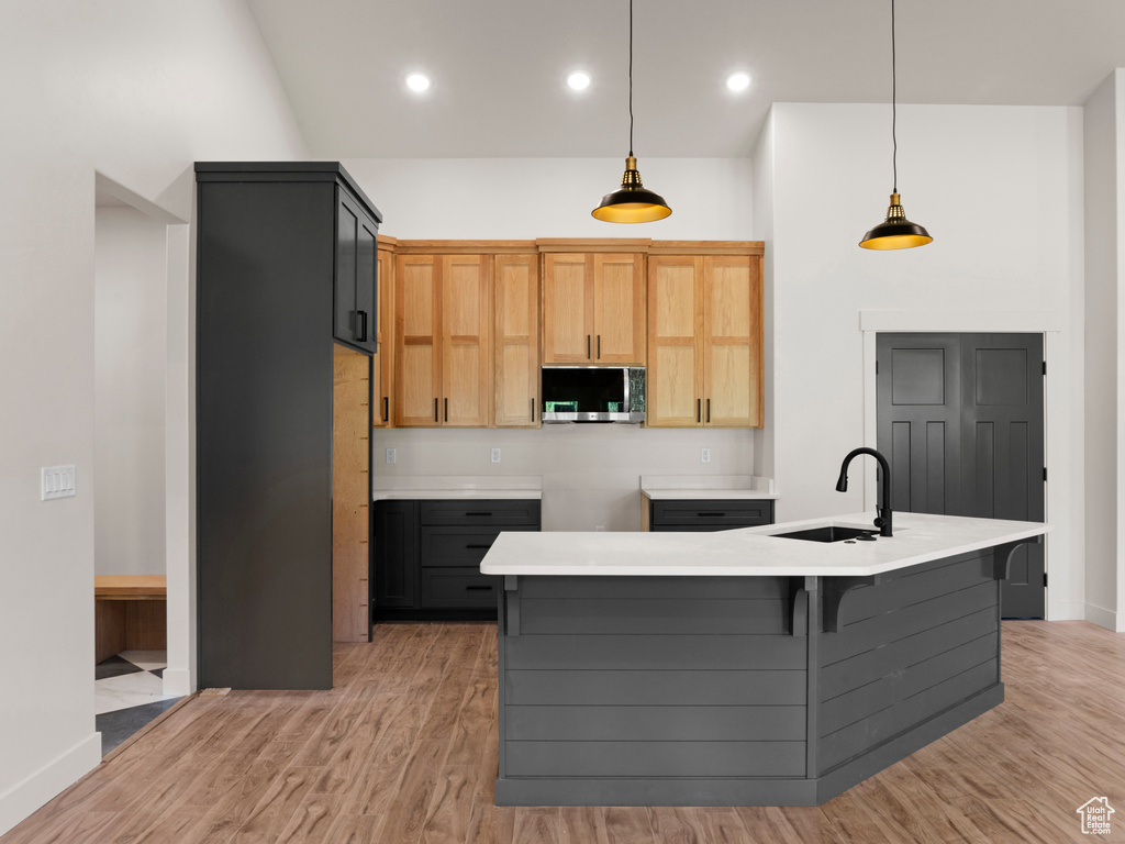 Kitchen with sink, light wood-type flooring, a kitchen island with sink, light brown cabinetry, and hanging light fixtures